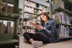 Asian female student sitting on floor in the library, Open and learning textbook from bookshelf